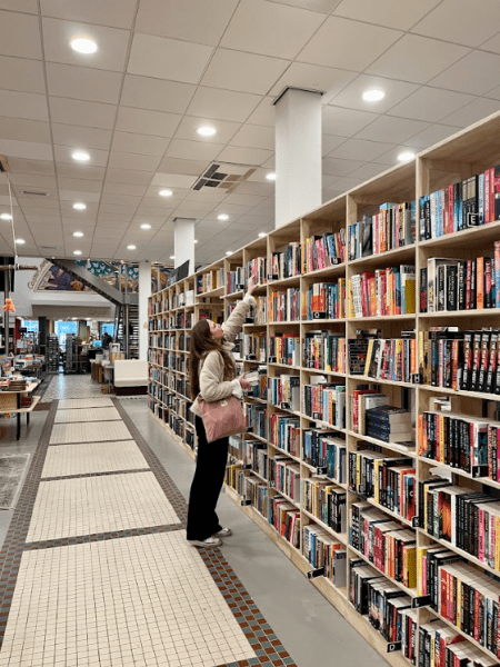 a woman in a bookstore stretching to the top shelf