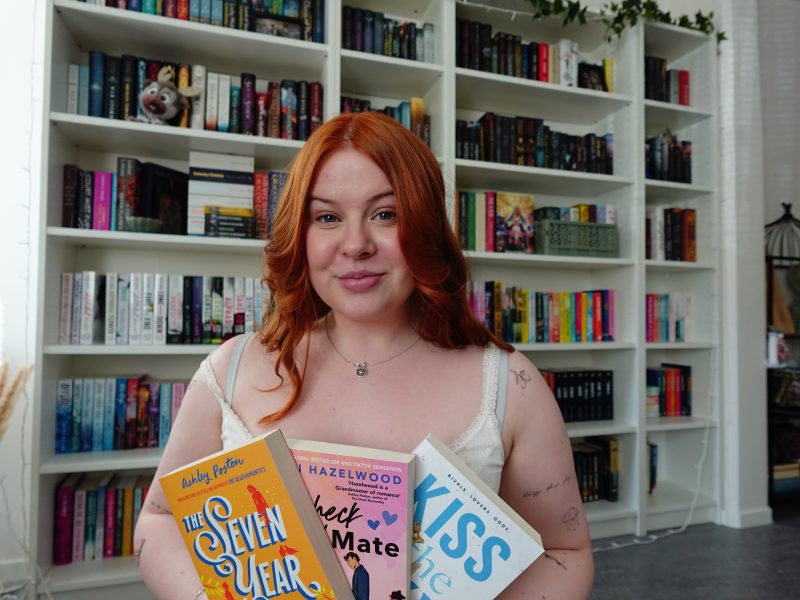a woman looking towards the camera holding 3 books