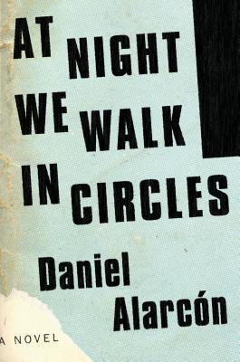 Book cover of the novel At Night We Walk in Circles by Daniel Alarcón, showing bold, irregular black block lettering on a textured light blue background with a stylized torn paper edge.